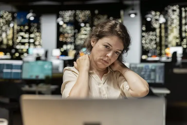 A woman rubs her neck while looking at her laptop computer.